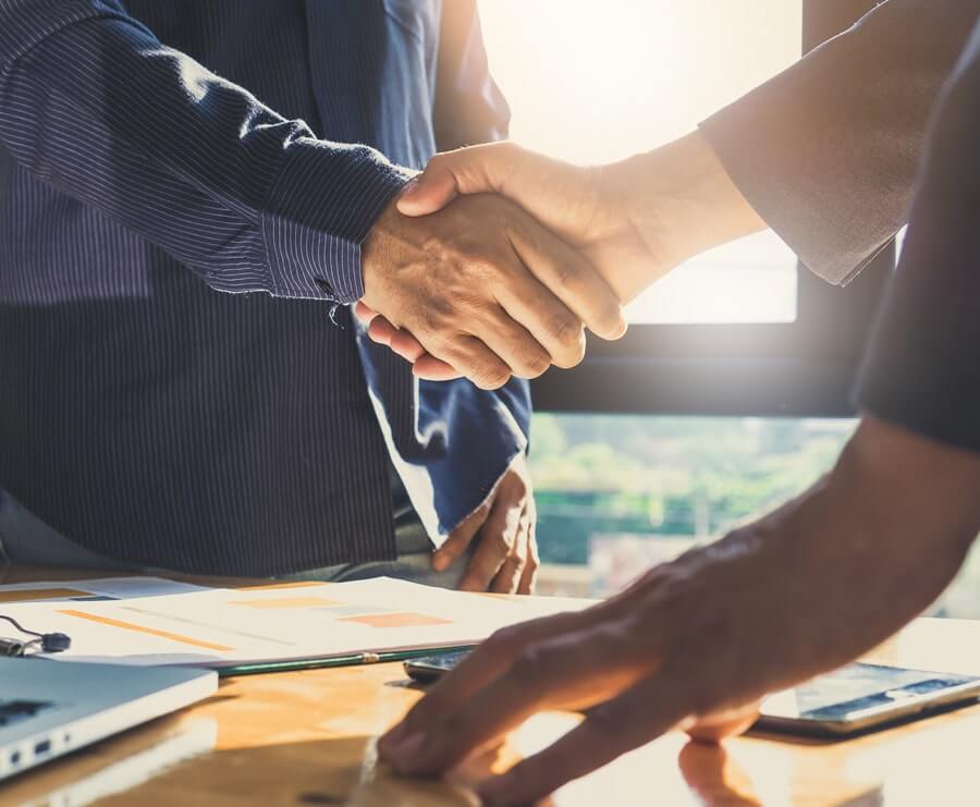 Image of a man in a suit shaking hands with someone else over a desk, their faces are out of frame